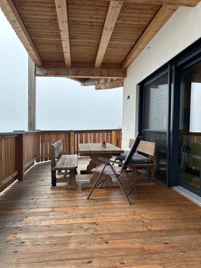 Großer Holzbalkon mit Sitzgelegenheiten und Blick auf die neblige Landschaft.