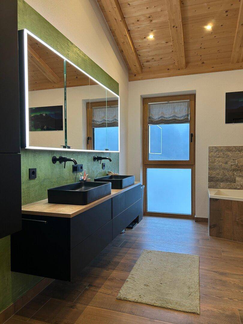 Elegantes Badezimmer mit Doppelwaschbecken, beleuchtetem Spiegel und Holzbalkendecke.