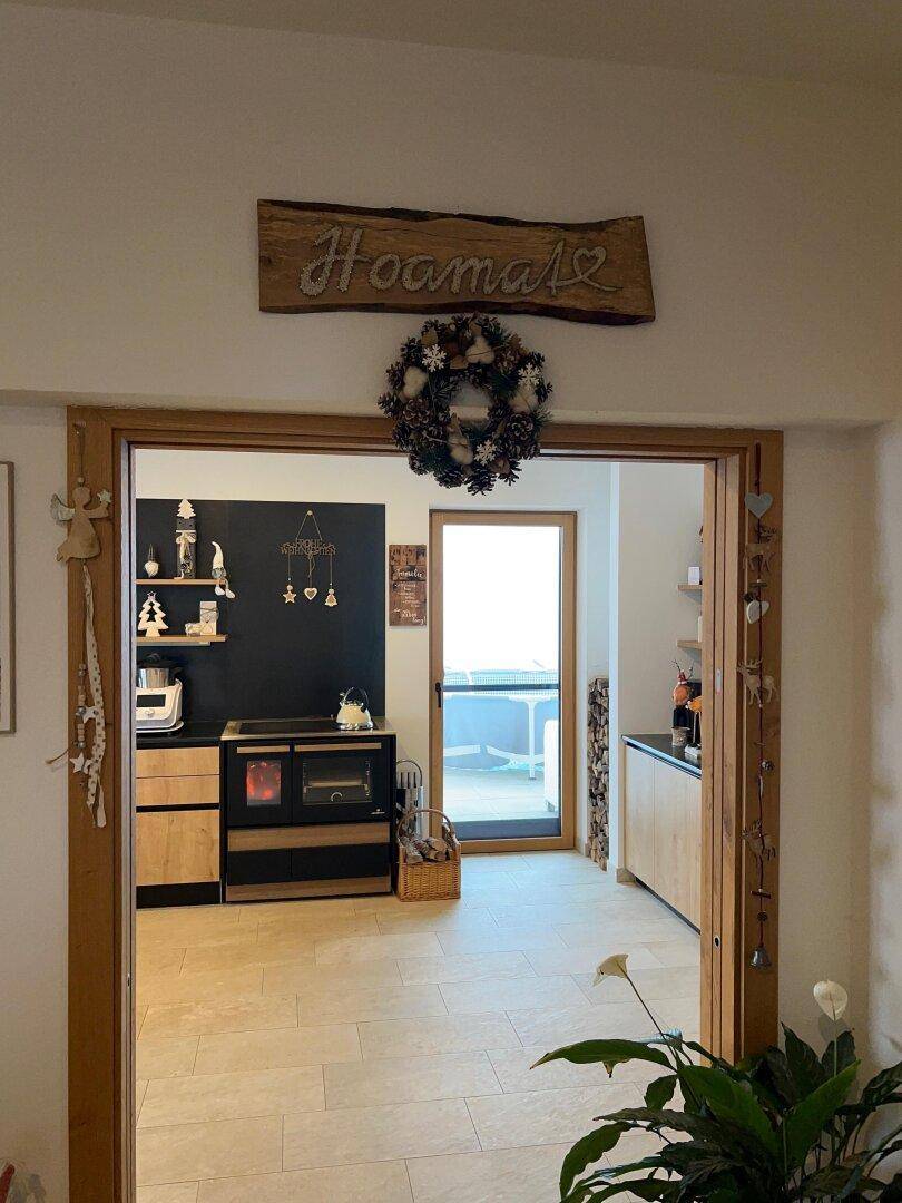 Gemütlicher Eingangsbereich mit Holztürrahmen und Blick in die moderne Küche mit Holzofen.