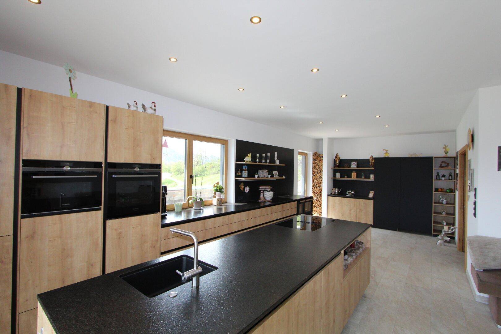 Geräumige, moderne Küche mit Holzschränken, dunkler Arbeitsplatte und integrierten Geräten.