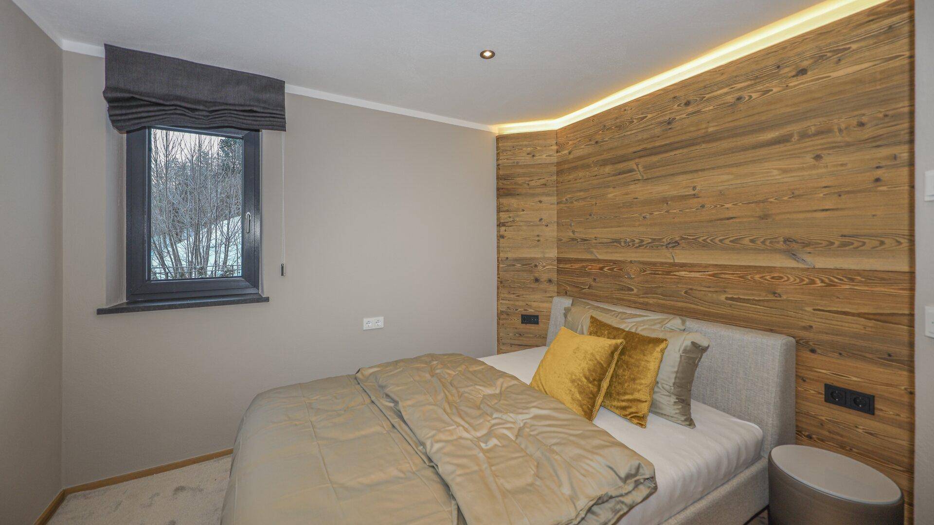 Gemütliches Schlafzimmer mit Holzwand, weichem Teppich und indirekter Beleuchtung.