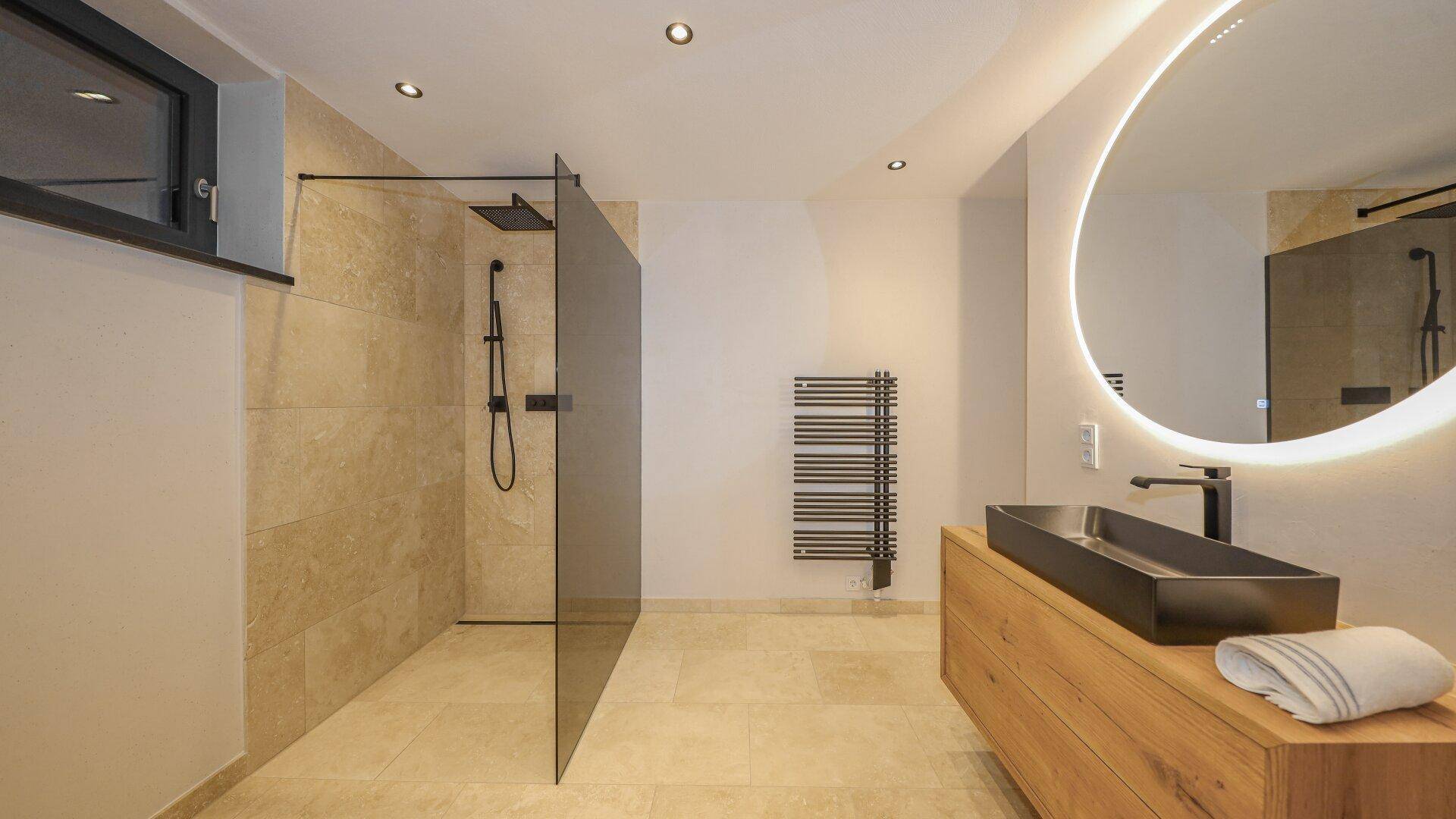 Modernes Badezimmer mit begehbarer Dusche, beleuchtetem Spiegel und beheiztem Handtuchhalter.