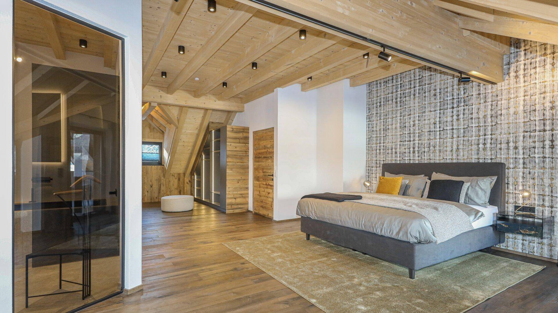 Geräumiges Schlafzimmer im Dachgeschoss mit Holzbalken, Holzboden und integriertem Kleiderschrank.