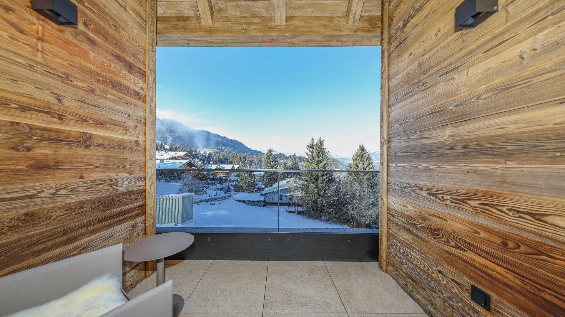 Gemütlicher Balkon mit Holzwänden und weitem Blick auf die verschneite Berglandschaft.