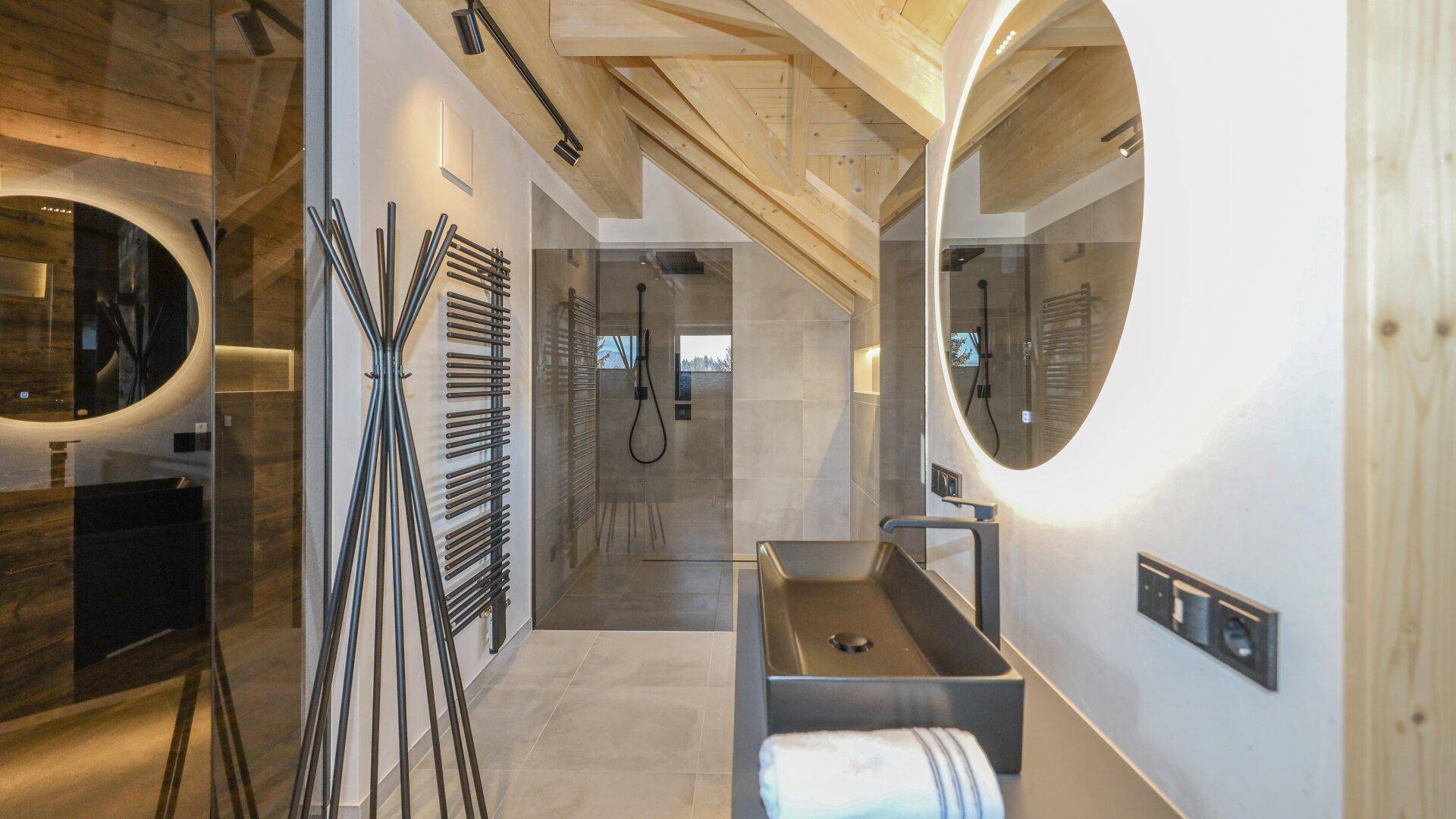 Modernes Badezimmer im Dachgeschoss mit begehbarer Dusche, Doppelwaschbecken und beleuchteten Spiegeln.