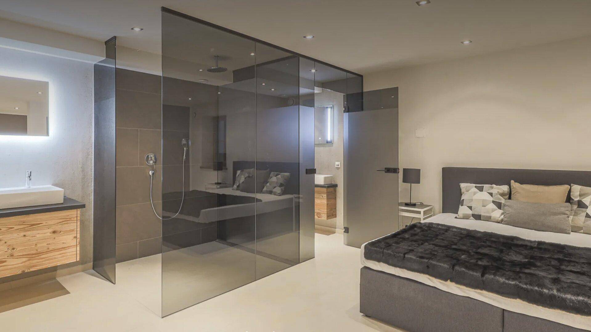 Schlafzimmer mit integriertem Badebereich, Glasdusche und modernem Waschbecken.