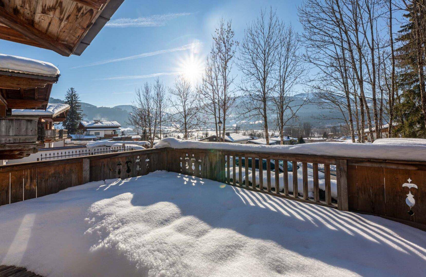 Verschneiter Balkon mit Holzbalkon und sonnigem Blick auf die winterliche Berglandschaft.