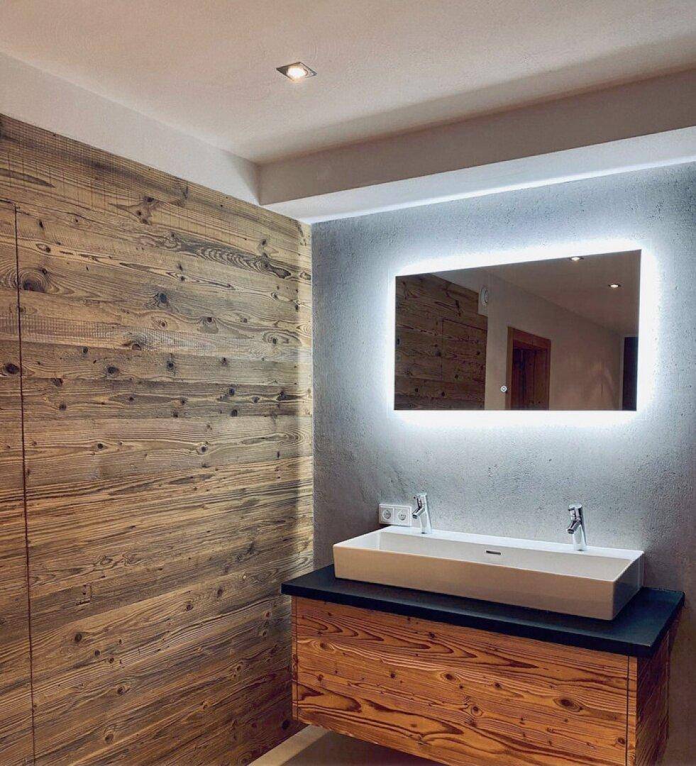 Modernes Badezimmer mit Holzvertäfelung, beleuchtetem Spiegel und elegantem Einzelwaschbecken.