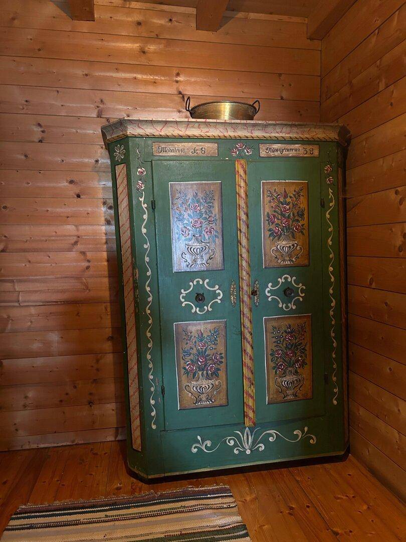 Traditioneller bemalter Holzschrank in einem Raum mit Holzwänden und rustikalem Teppich.