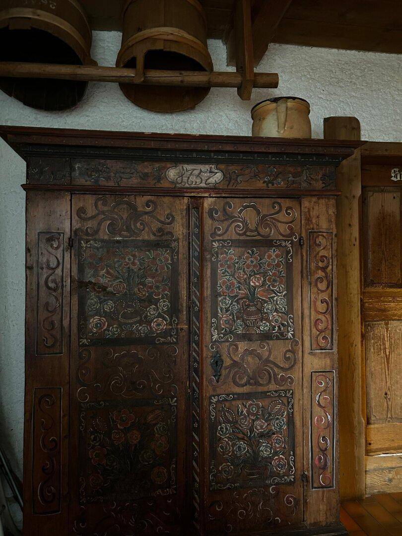Alter, kunstvoll bemalter Holzschrank in einem traditionellen Raum mit Holzwänden.