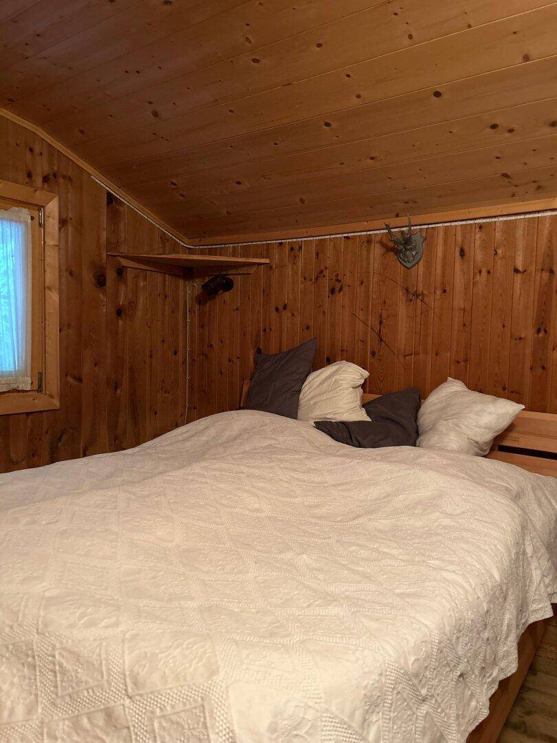 Gemütliches Schlafzimmer mit Holzwänden, Holzbett und Hirschgeweih als Dekoration.