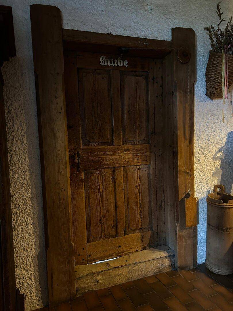 Rustikale Holztür mit traditioneller Beschriftung "Stube" in einem Flur mit Terrakotta-Fliesen.
