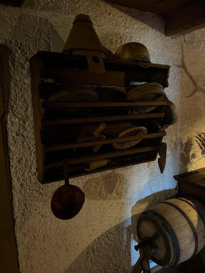 Wandregal mit traditionellen Dekorationsgegenständen und einem Holzfass in einem rustikalen Ambiente.