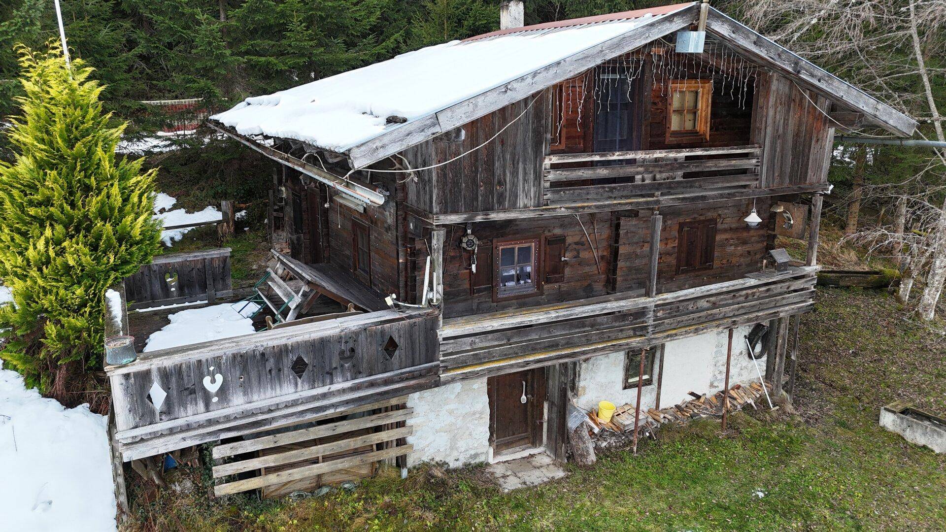Rustikales Holzhaus mit Balkon und schneebedecktem Dach, eingebettet in eine winterliche Landschaft.