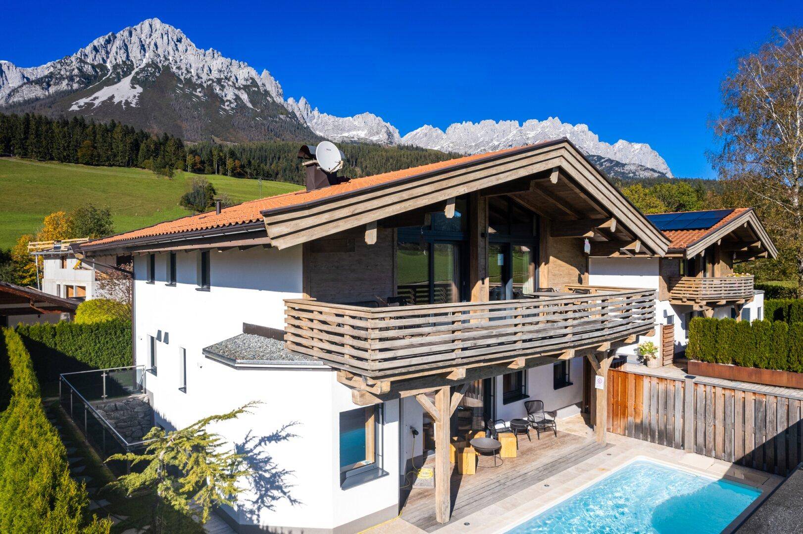 Modernes Chalet mit Pool, Balkon und Bergblick an einem sonnigen Tag.