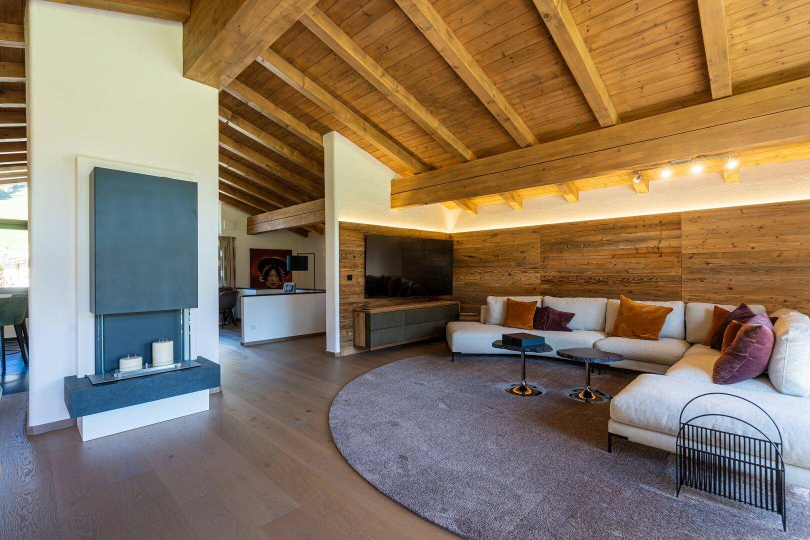 Gemütlicher Wohnbereich mit Holzbalkendecke, modernem Kamin und großem Sofa.