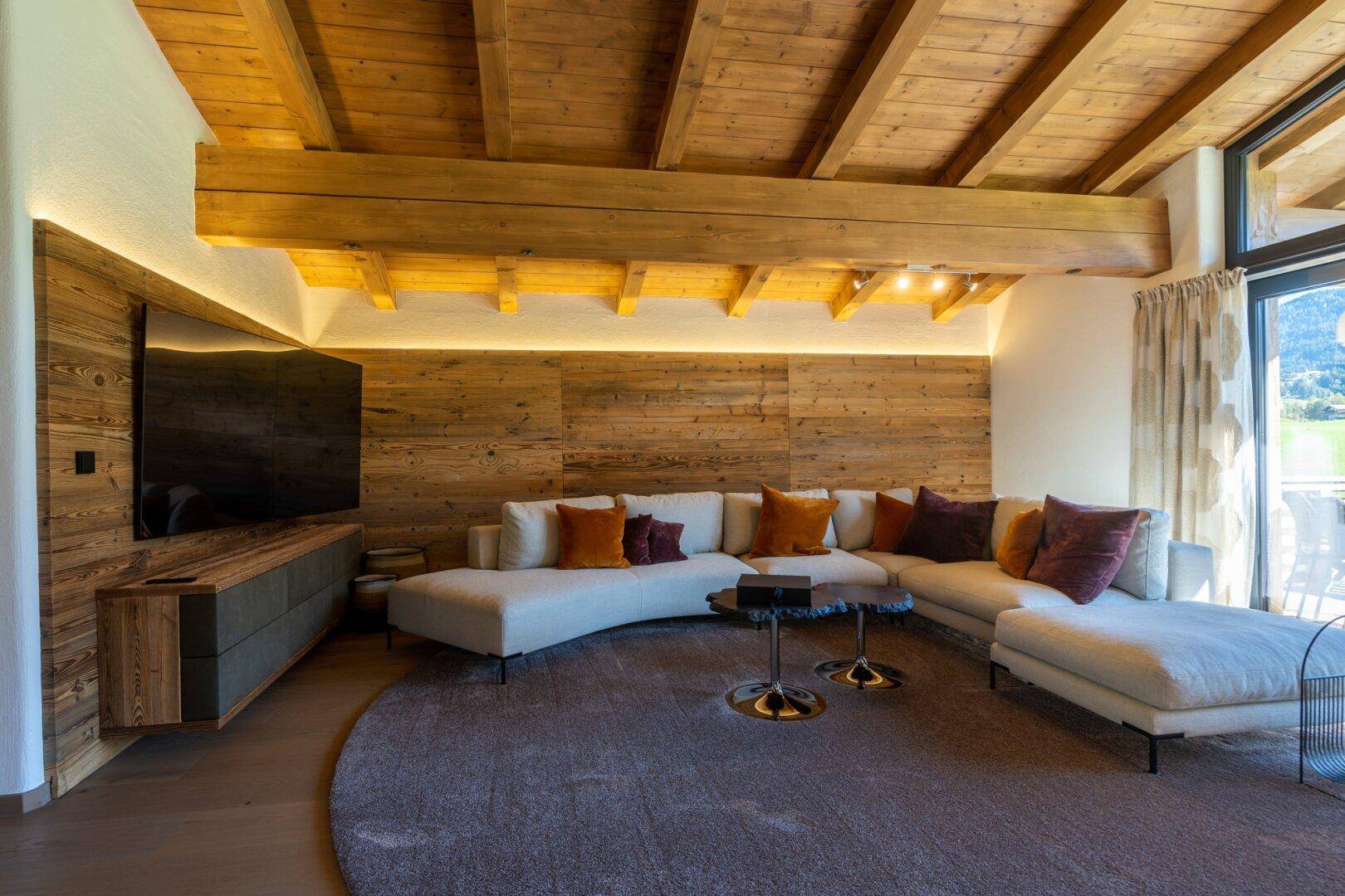 Lichtdurchfluteter Wohnbereich mit Holzwand, großem Sofa und Zugang zum Balkon.