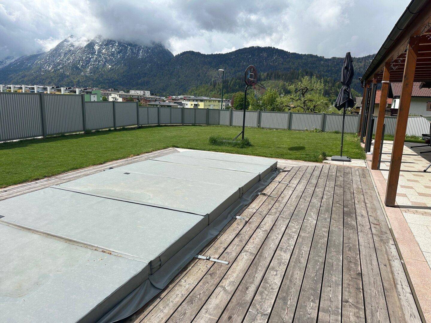 Großer Garten mit Holzdeck, abgedecktem Pool und Bergblick im Hintergrund.