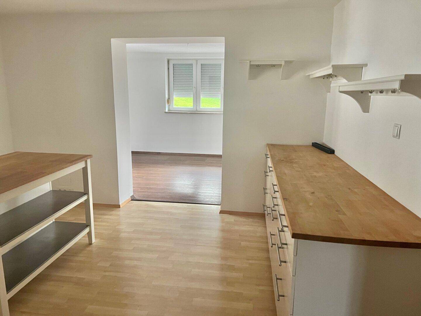 Offener Bereich mit Holzboden und Blick in einen angrenzenden Raum mit Fenster.