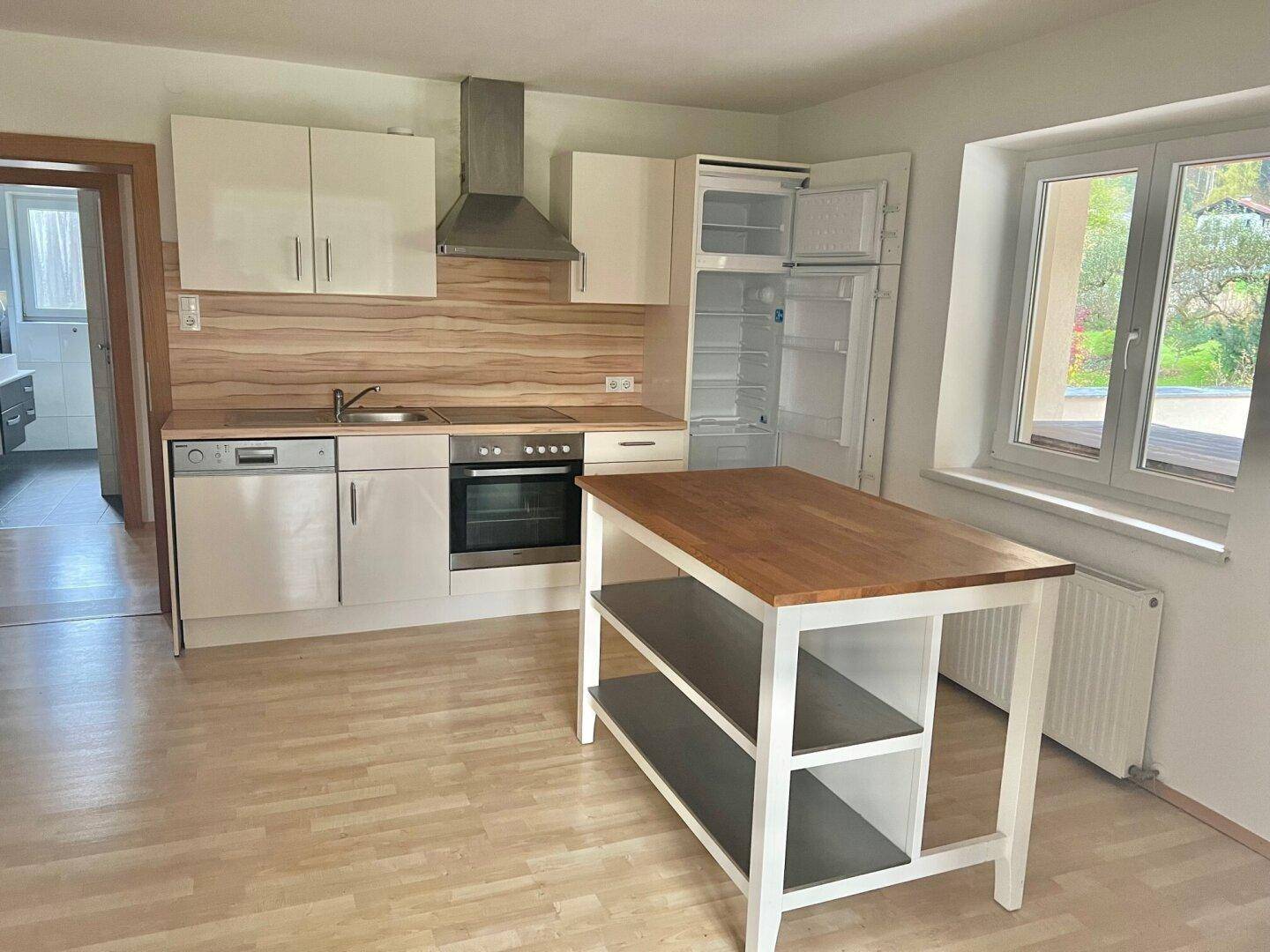 Funktionale Küche mit weißen Schränken, Holz-Arbeitsplatte, Kücheninsel und Fenster.