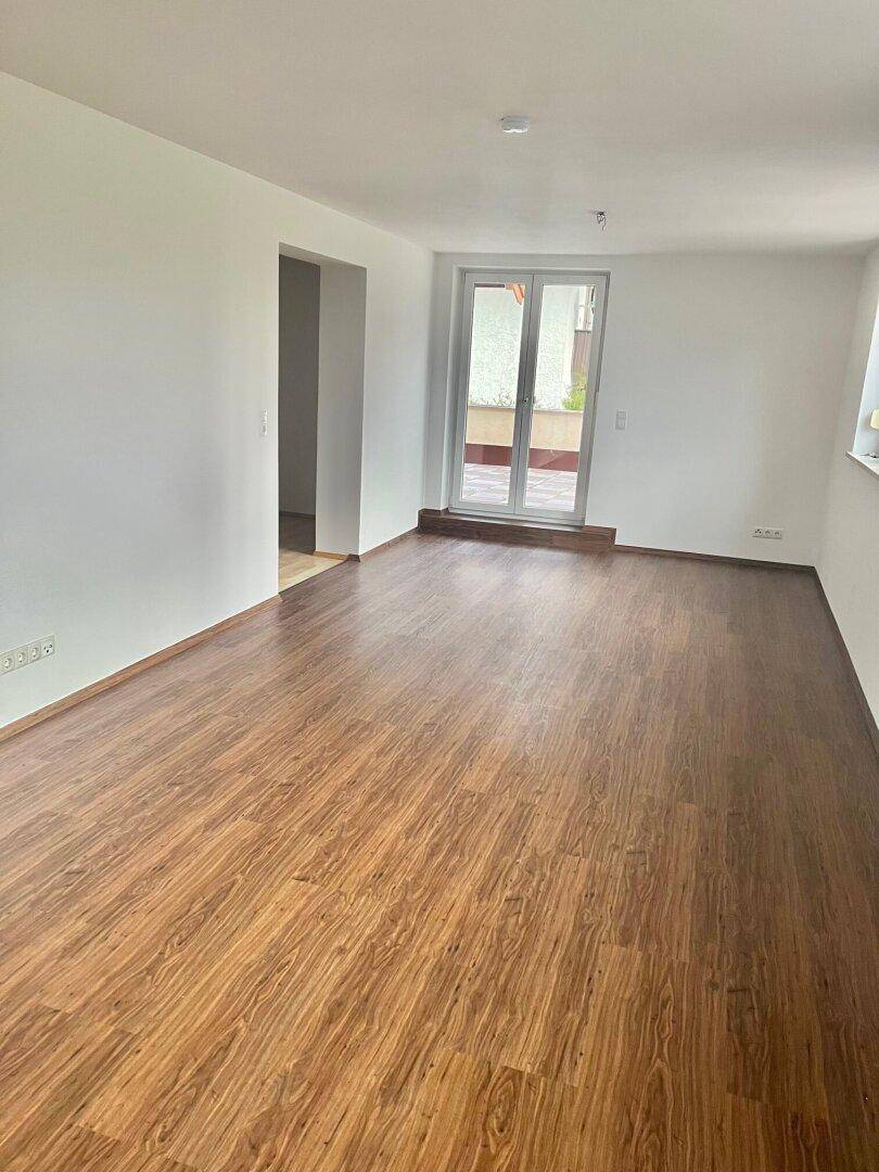 Leeres Wohnzimmer mit Holzboden und Zugang zu einem Balkon oder einer Terrasse.