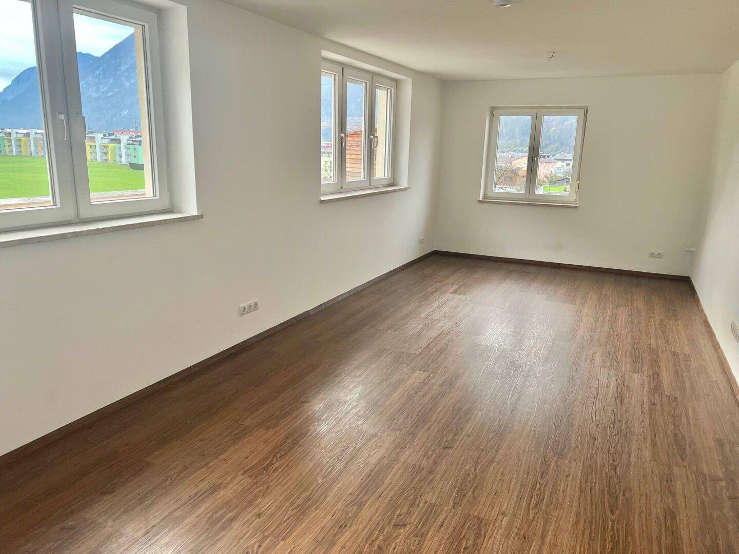 Helles Wohnzimmer mit Holzboden und mehreren Fenstern, die einen weiten Blick bieten.