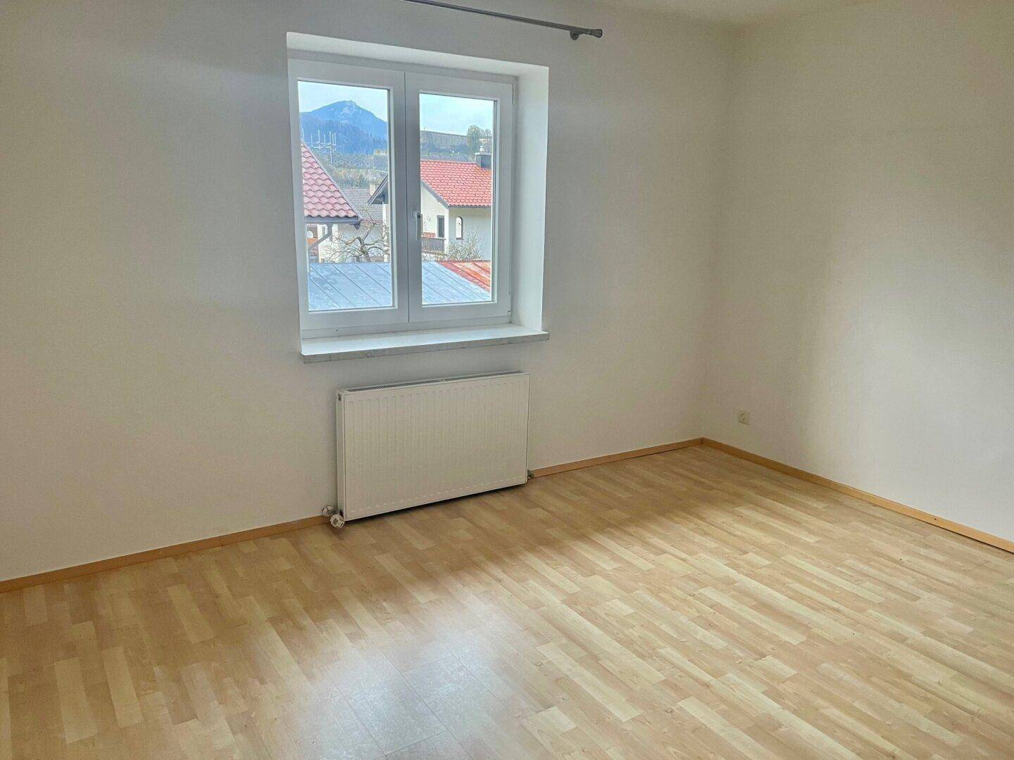 Helles Schlafzimmer mit Holzboden und einem Fenster, das einen Blick nach draußen ermöglicht.