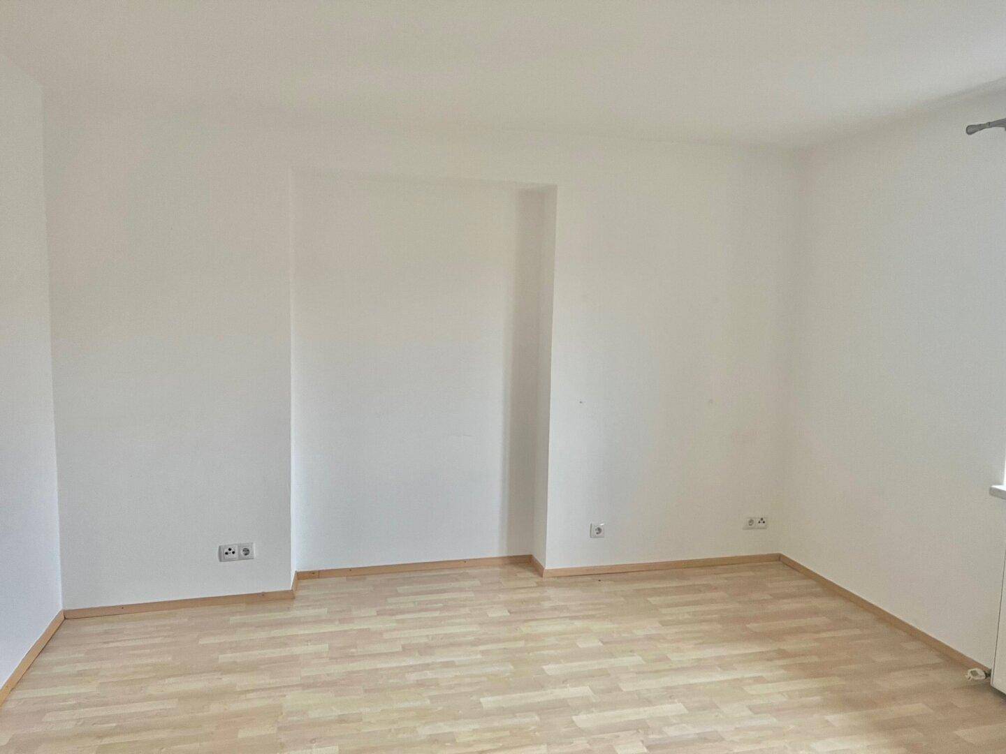 Leeres Schlafzimmer mit Holzboden und weißen Wänden, bereit zur individuellen Gestaltung.