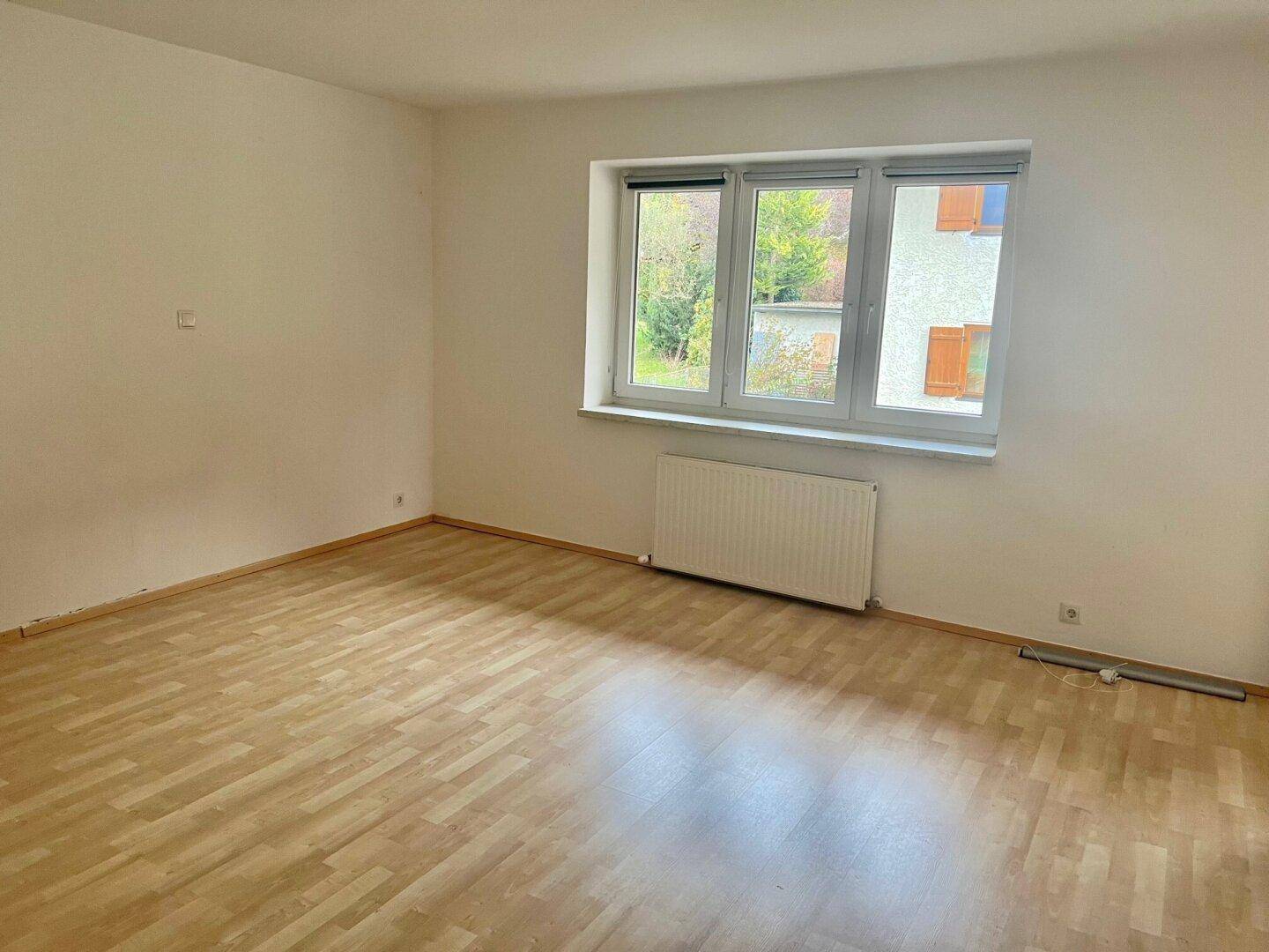 Helles Schlafzimmer mit Holzboden und einem großen Fenster mit Blick ins Grüne.