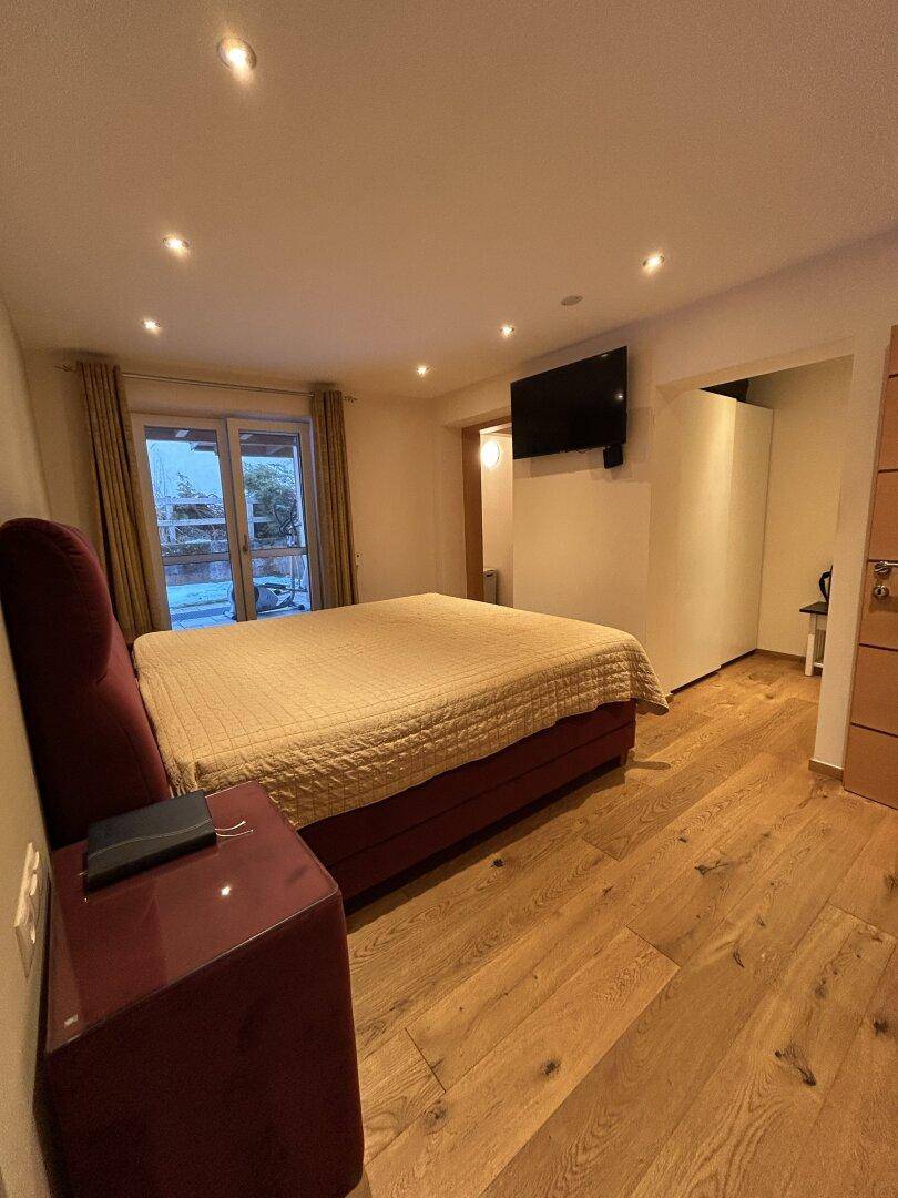 Schlafzimmer mit großem Bett, Holzboden und Zugang zu einem Außenbereich.