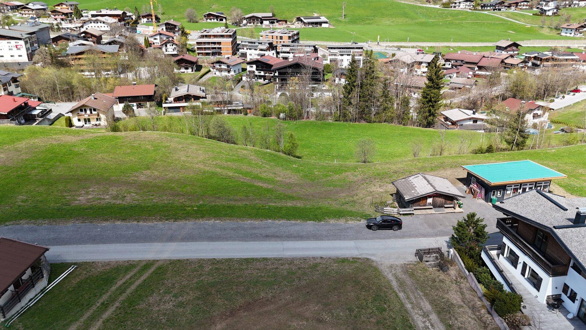 Luftaufnahme einer ländlichen Straße, umgeben von sanften grünen Hügeln und vereinzelten Gebäuden in der Natur.