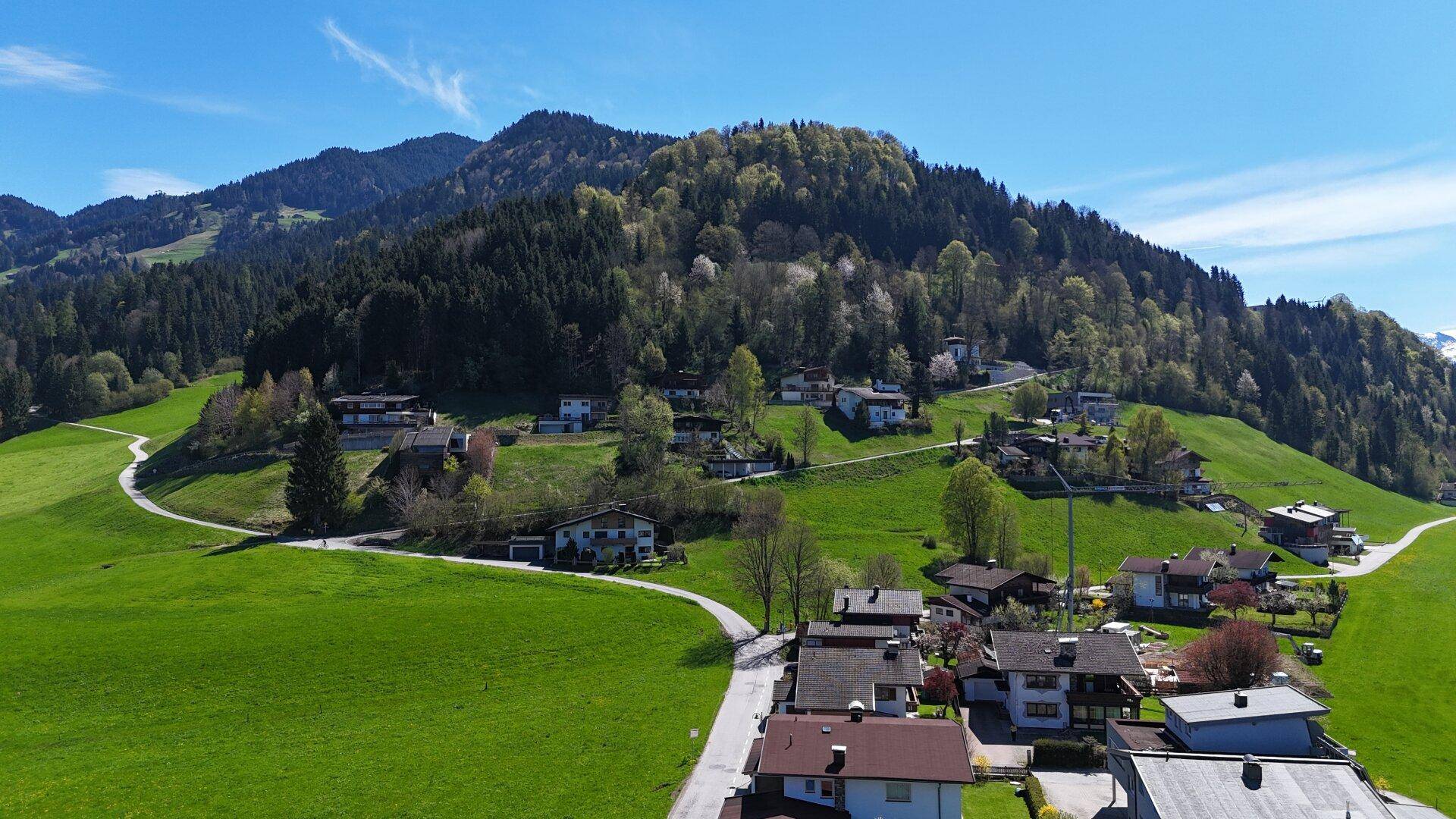 Luftaufnahme eines malerischen Dorfes eingebettet in grüne Hügel und bewaldete Berge.