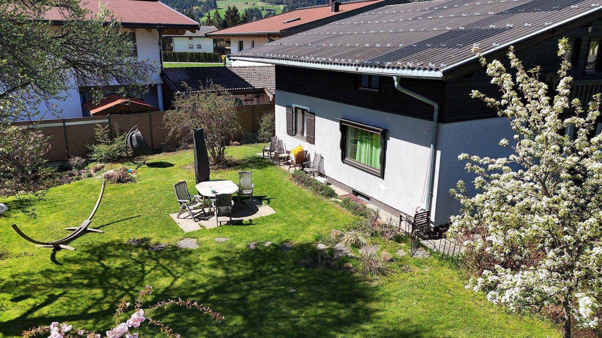 Erhöhte Ansicht des Gartens mit Sitzbereich, Hängematte und der Hausfassade im Hintergrund.