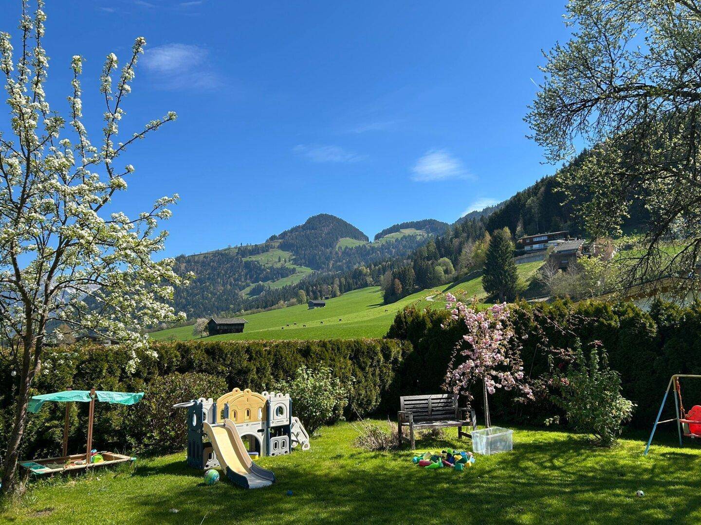Geräumiger Garten mit Kinderspielplatz, Sitzbank und weitem Blick auf die grünen Berge.