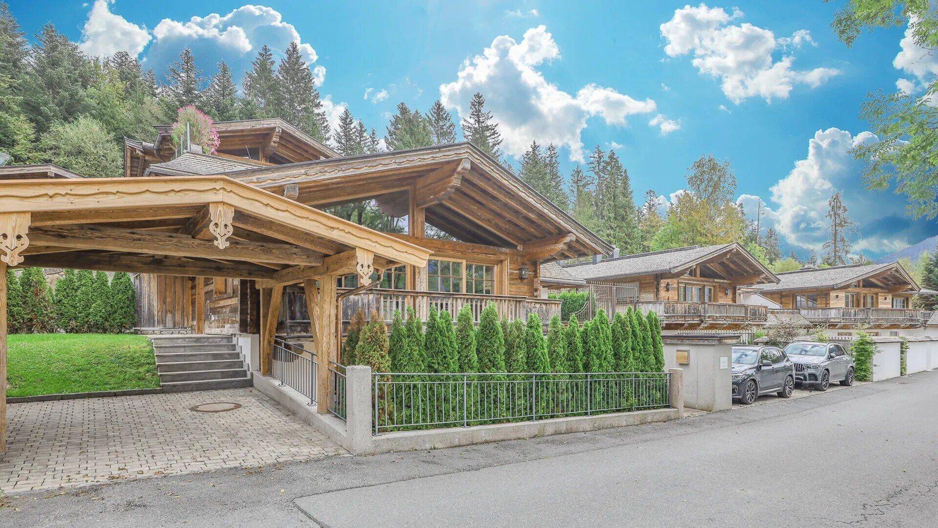 Traditionelle Chalet-Architektur mit Holzbalkonen, Carport und gepflegter Außenanlage in alpiner Umgebung.