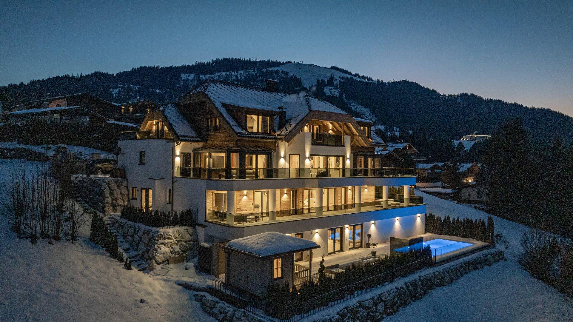 Luxuriöses Anwesen in den Bergen bei Nacht mit beleuchteten Balkonen und einem beheizten Außenpool.