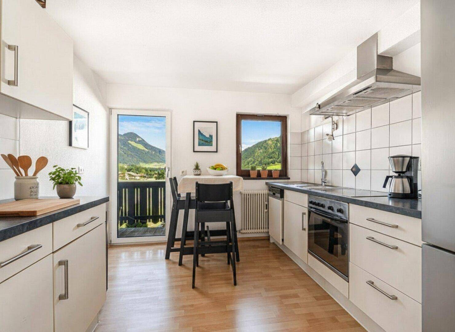 Helle Küche mit weißen Schränken, Esstisch und Balkonzugang mit Bergblick.