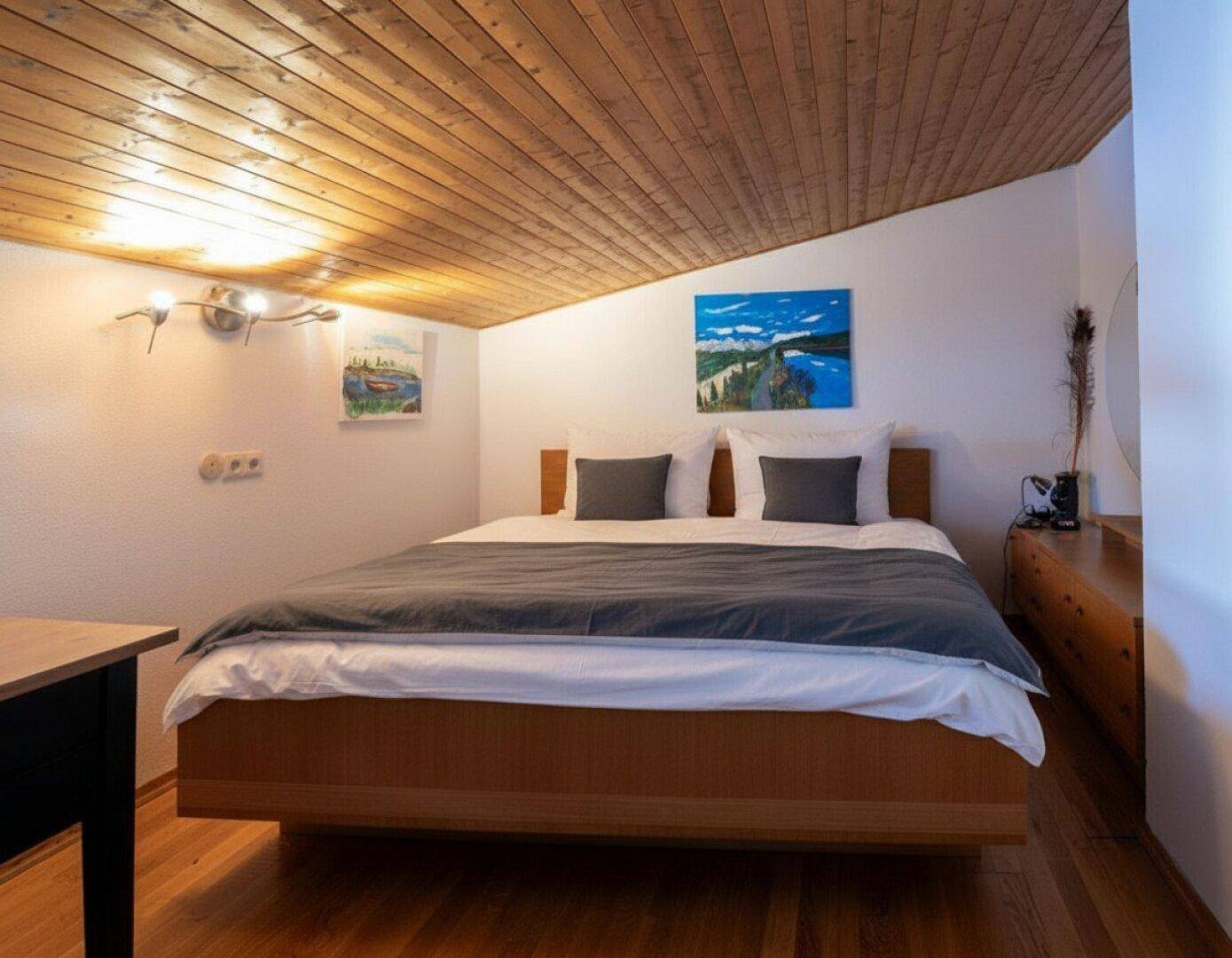 Schlafzimmer mit Holzbett, schräger Holzdecke und weiß gestrichenen Wänden.