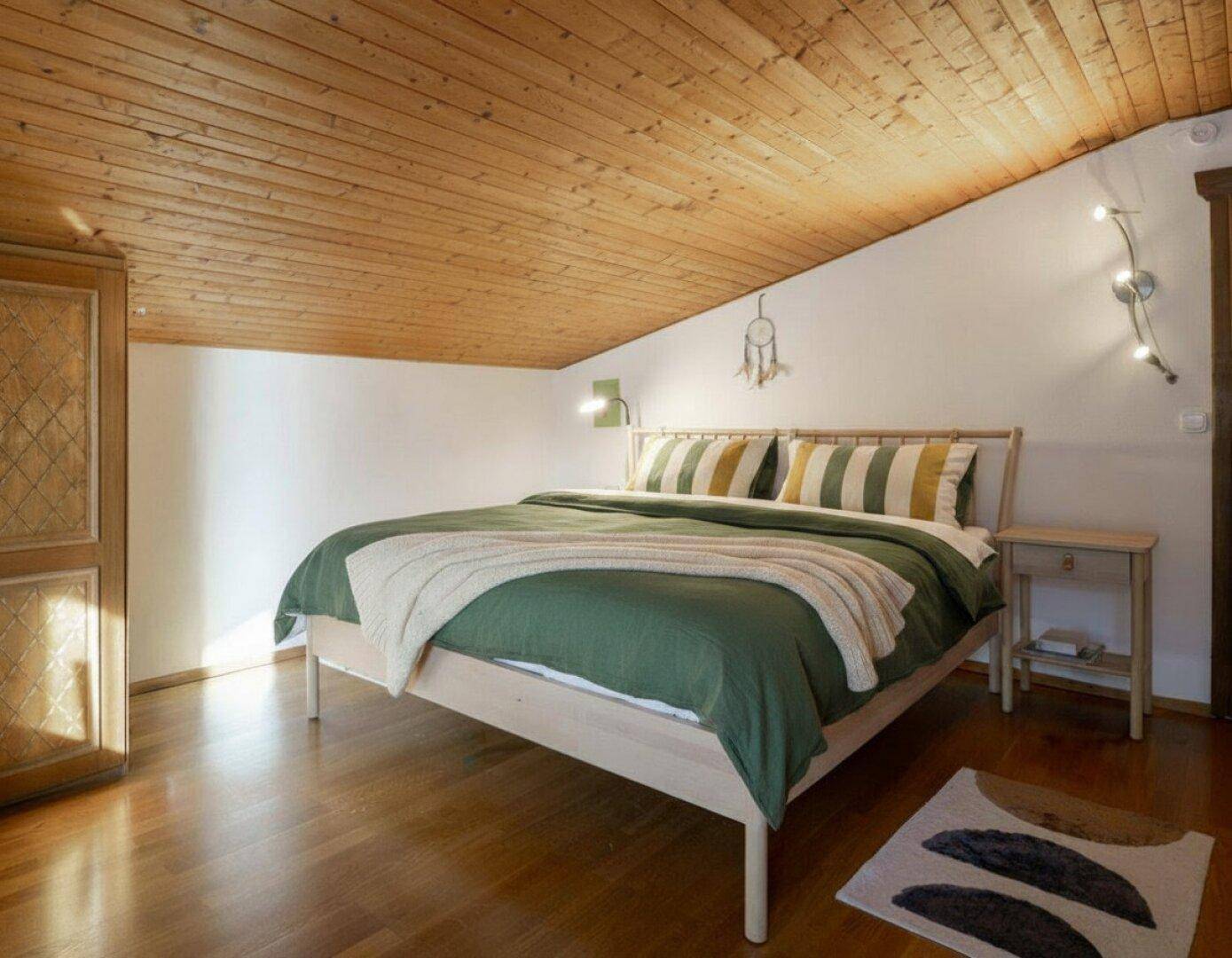 Gemütliches Schlafzimmer mit Holzbett, Holzdecke und schrägen Wänden im Dachgeschoss.