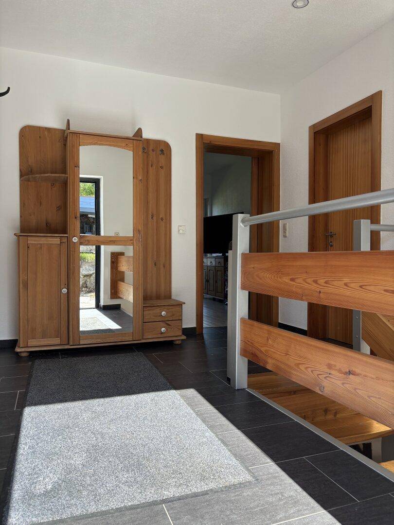 Eingangsbereich mit dunklen Fliesen, Holzgarderobe und Treppe zu den oberen Etagen.