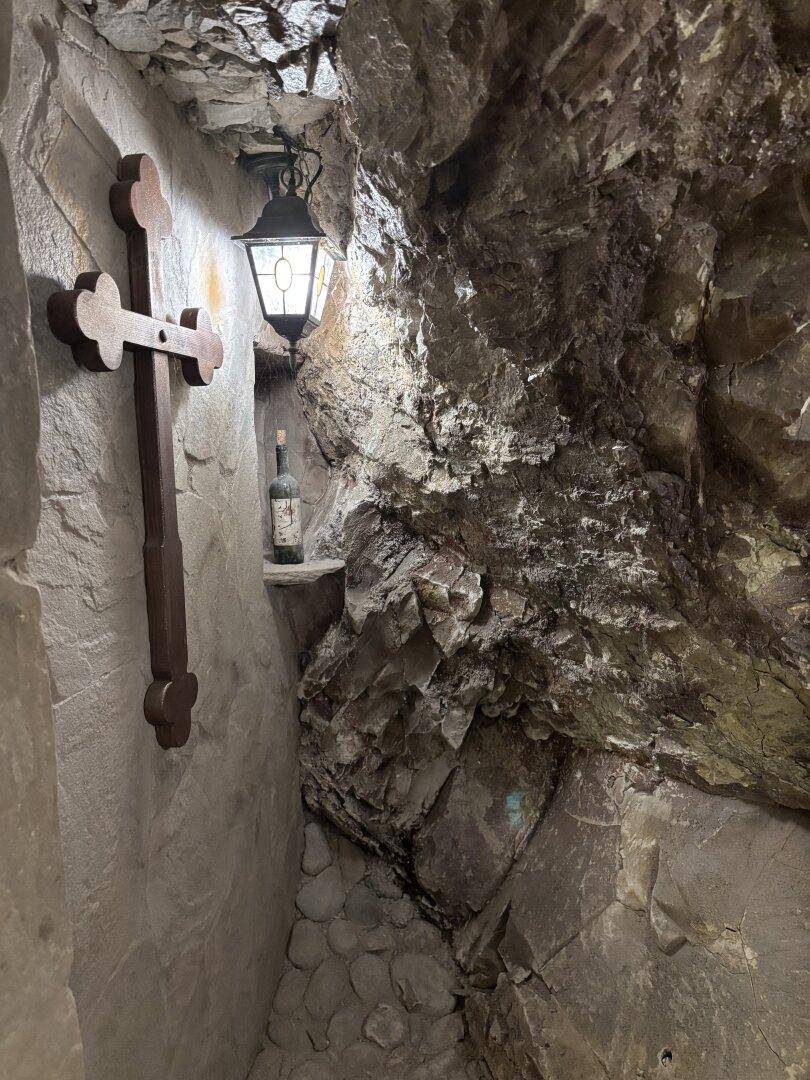 Historischer Weinkeller mit rauen Steinwänden, Holzkreuz und stimmungsvoller Beleuchtung.