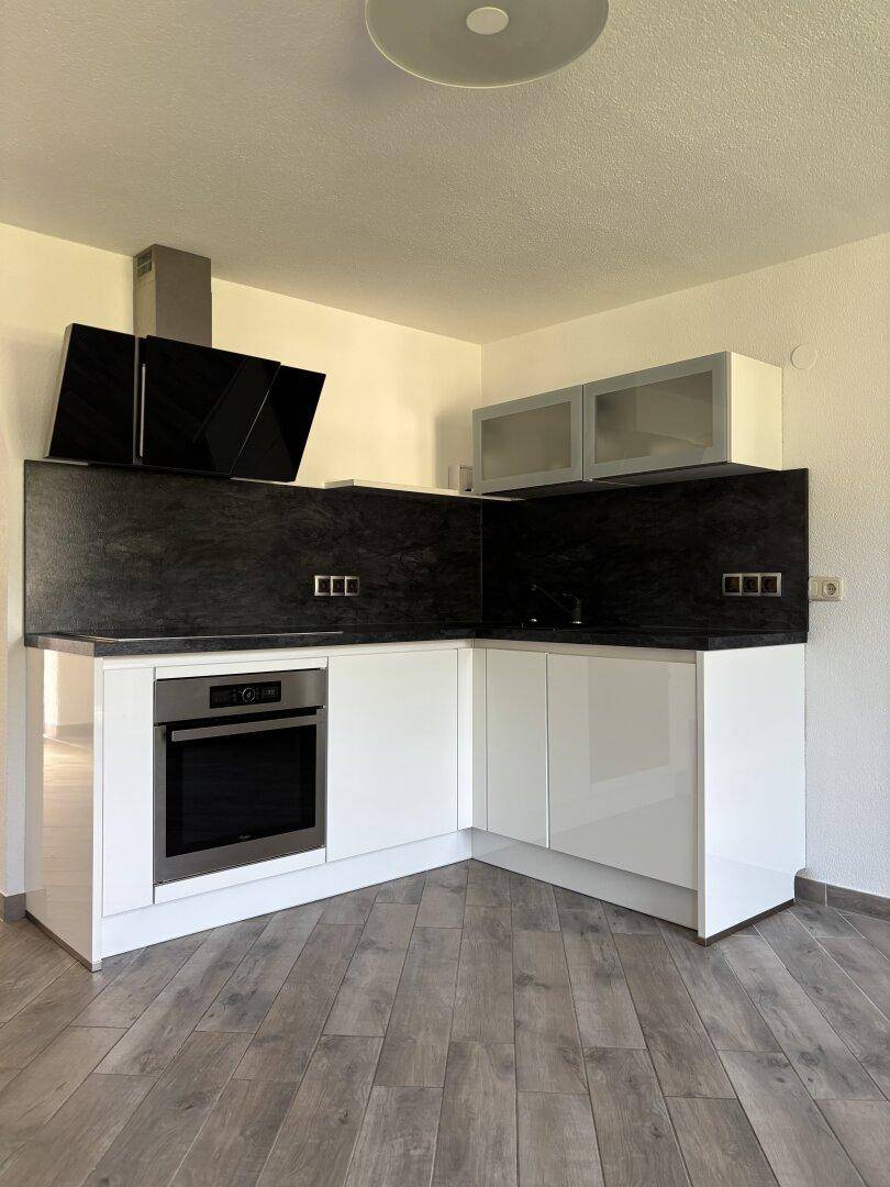 Moderne Küchenzeile mit weißen Hochglanzfronten, schwarzer Rückwand und integriertem Backofen.