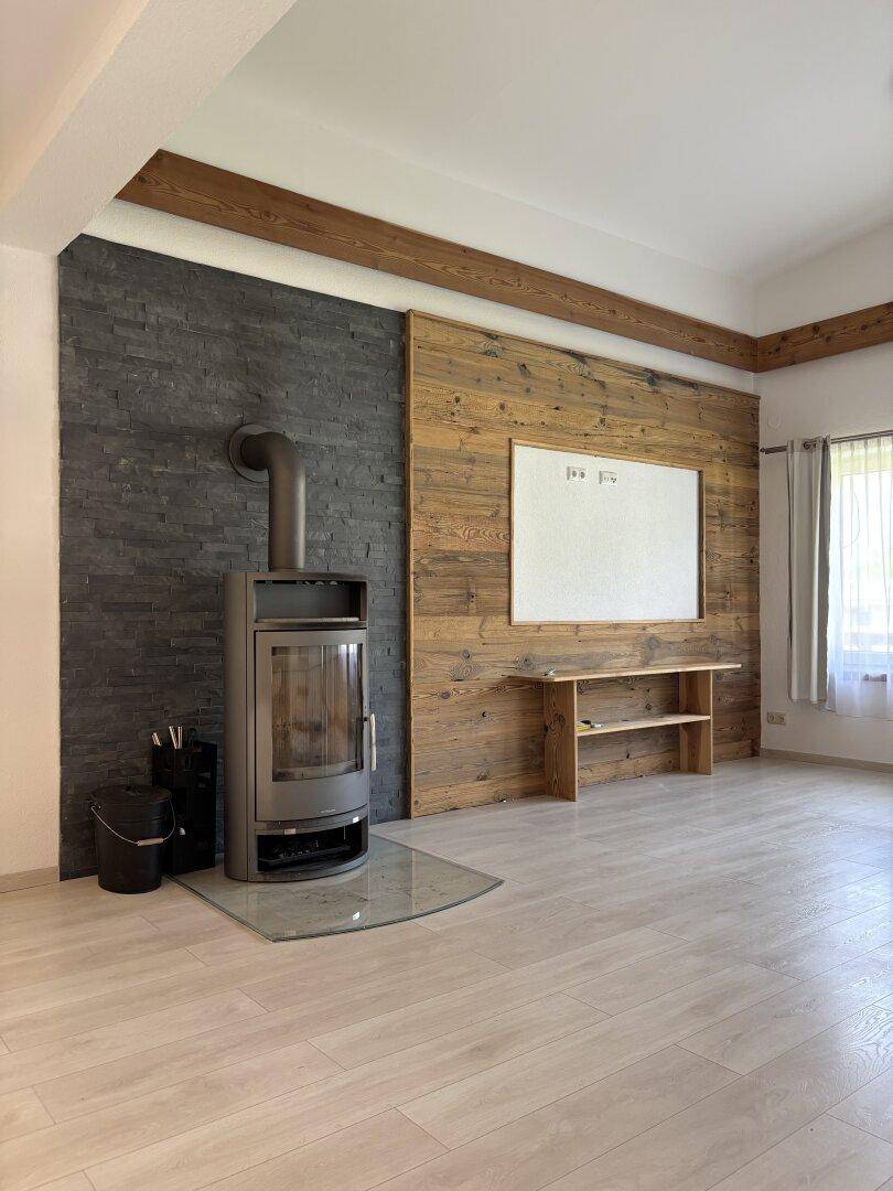 Gemütliches Wohnzimmer mit Kaminofen, Steinwand und Holzakzenten sowie sichtbaren Deckenbalken.