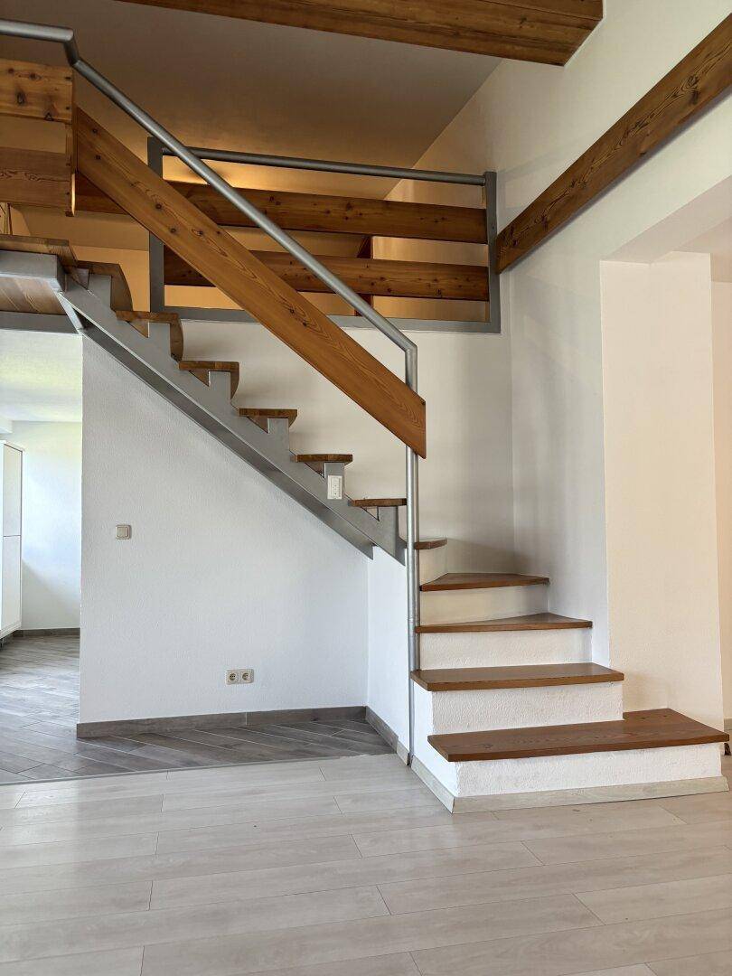 Offene Holztreppe mit Metallgeländer und sichtbaren Holzbalken, die zu einer Galerie führt.