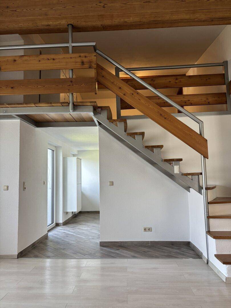 Offene Holztreppe mit Metallgeländer, die zu einem weiteren Wohnbereich führt.