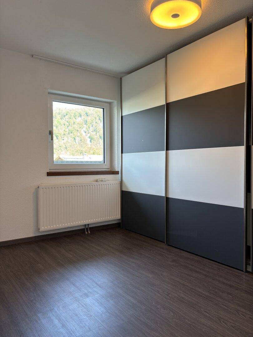 Schlafzimmer mit dunklem Laminatboden, Fenster und einem großen Schiebetürenschrank.