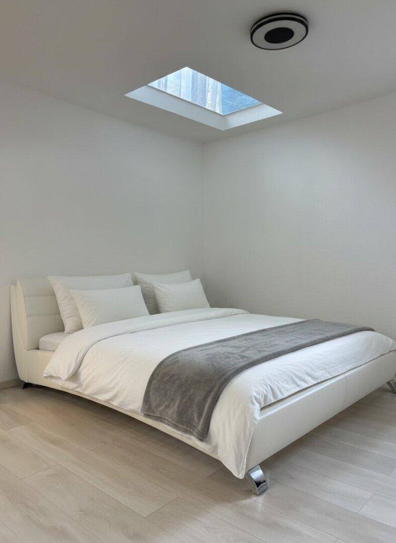 Helles Schlafzimmer mit weißem Bett, Laminatboden und einem Dachfenster für natürliches Licht.