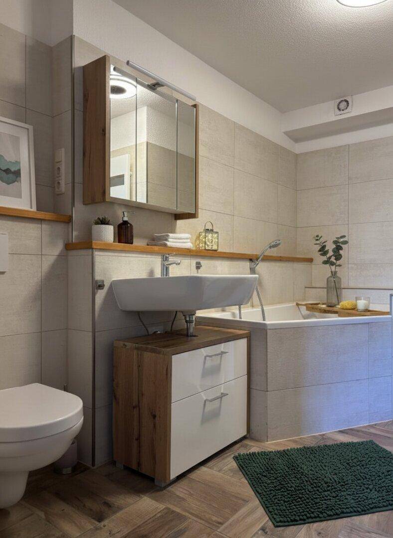 Modernes Badezimmer mit Badewanne, Waschtisch und hellen Fliesen an Wänden und Boden.