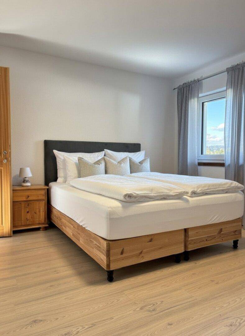 Helles Schlafzimmer mit Holzbett, Nachttisch und Fenster mit Blick ins Grüne.