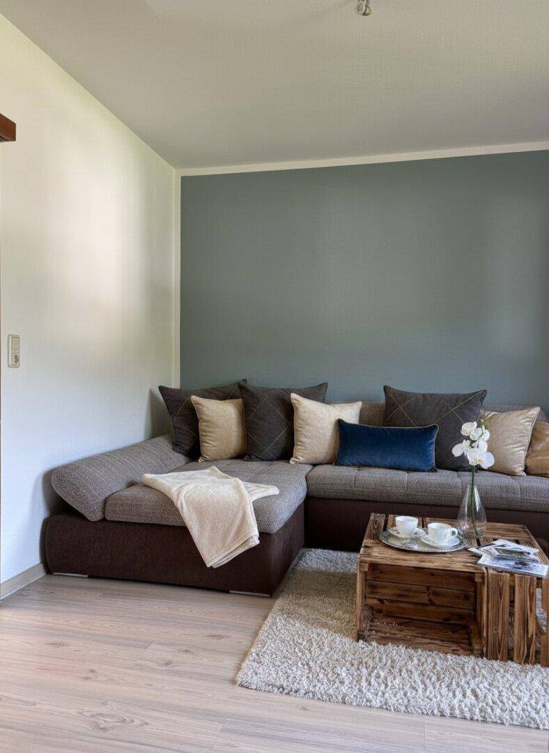 Gemütliches Wohnzimmer mit großem Ecksofa, Holztisch und einer farbigen Akzentwand.
